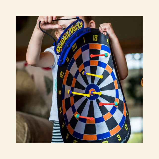 Child holding the Doinkit Darts Rollup Magnetic Dartboard during family game play.