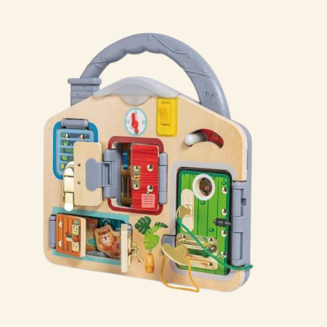 Hape Lock & Learn Playboard shown out of the box with a wooden carry handle, colorful doors, key lock, chain latch, bolt, buckle, hook lock, analog clock, light switch, and wooden cat hiding behind a door.