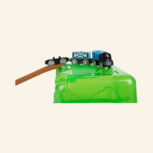 Hape Railway Bucket Builder Set green storage bucket used as a hill, with a wooden track ramp leading to the top and a train car traveling across the elevated section.