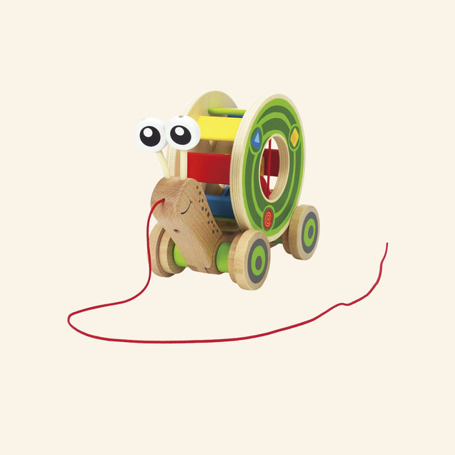 Hape Walk-A-Long Snail shown from the front with a wooden snail body, red pull string, colorful rolling shell, green wheels, and friendly eye stalks.
