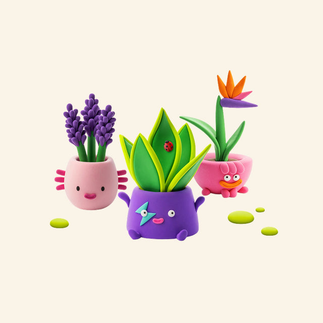 Three completed Hey Clay Plant Folks creations including a bird of paradise, snake plant, and salvia plant in colorful character pots.