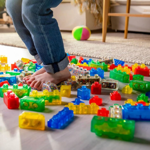 Colorful building blocks on a floor with a child's legs and feet in jeans.