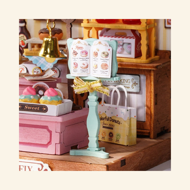 Rolife Sweetie’s Donut Shop miniature scene shown close up with donut display case, menu board, bakery counter, pastel shop details, and tiny dessert accessories.