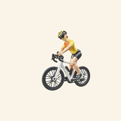 Bruder cyclist figure riding a white road bike, shown wearing yellow riding gear, helmet, sunglasses, black shorts, and detailed cycling shoes.