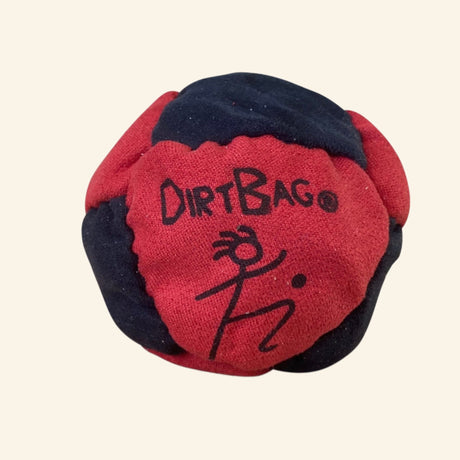 Dirtbag Classic Footbag in red, navy, and black synthetic suede panels with the Dirtbag logo and stick-figure artwork printed on the red center panel.