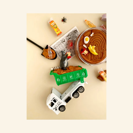 Earth Grown KidDoughs Garbage KidDough Play Kit shown from above with a green garbage truck, raccoon figure, brown scented dough, shovel, banana peel, toy bugs, bottles, and pretend garbage pieces arranged for sensory play.
