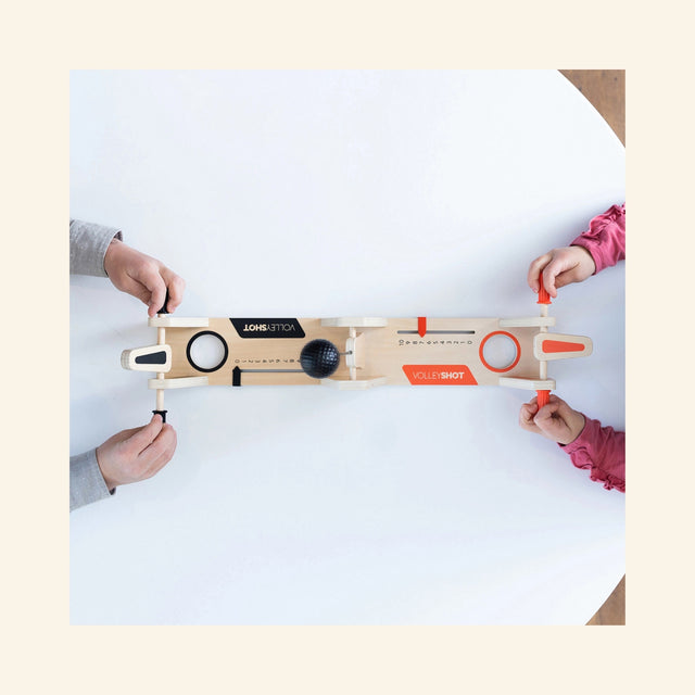 Overhead play view of Fat Brain Toys VolleyShot Game with two players’ hands on the paddle controls as the attached ball moves across the tabletop game.