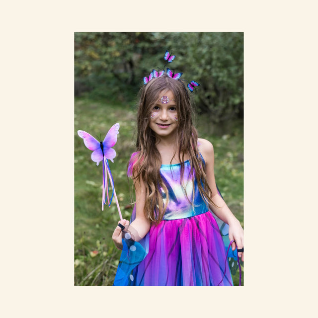 Child wearing a colorful butterfly-inspired dress and holding the Great Pretenders Float Like a Butterfly Wand outdoors.
