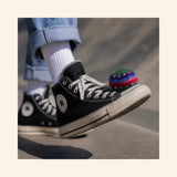 Colorful Guatemalan foot bag resting on the toe of a black high-top sneaker during outdoor play.