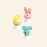 Hape Cheery Critter Rattle Trio shown out of the box with yellow chick, pink rabbit, and teal mouse rattles, each on a white suction cup base with soft silicone teething ears.
