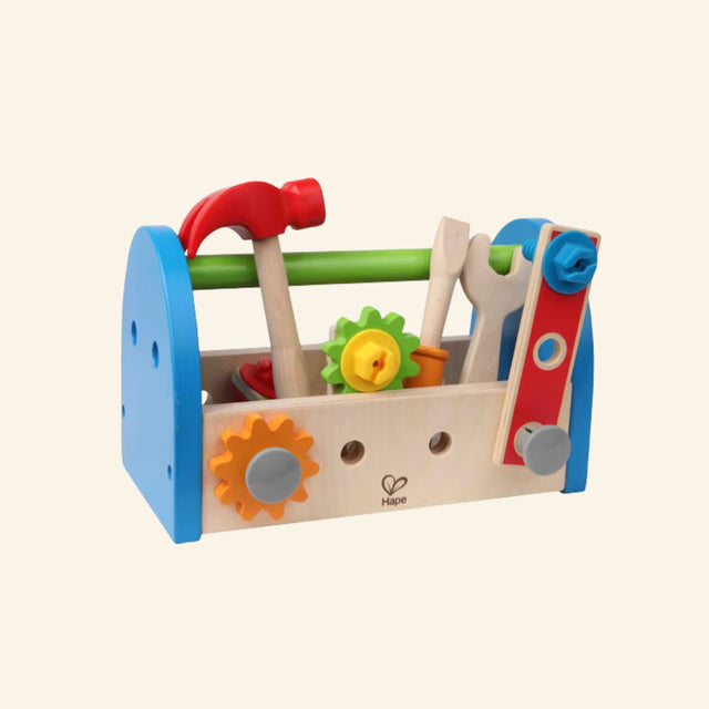 Hape Fix-It Tool Box shown assembled with a wooden toolbox, blue side panels, green handle, red hammer, screwdriver, wrench, ruler, gears, links, bolts, and nuts stored inside.