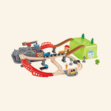 Hape Railway Bucket Builder Set shown fully assembled with wooden train tracks, red bridge, green storage bucket hill, gray mountain lid, crane, train cars, signs, trees, and cargo pieces.
