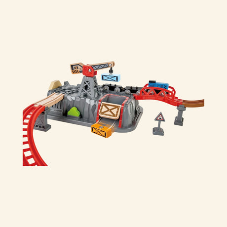 Hape Railway Bucket Builder Set track layout detail showing wooden rails, red bridge pieces, gray mountain lid, magnetic crane, cargo crate, signs, and train cars.