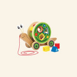 Hape Walk-A-Long Snail shown with the wooden snail body, colorful shape-sorting shell, red pull string, and three loose shape blocks in yellow, red, and blue.