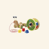 Hape Walk-A-Long Snail shown from the side with the red pull string, wooden snail body, green wheels, colorful rolling shell, and shape sorter blocks nearby.