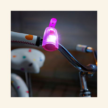 Pink Horn Brightz LED bike horn attached to bicycle handlebars glowing with colorful lights during use.
