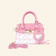 Hot Focus Charmie Luxe Crossbody – Bowtiful mini handbag shown in pink textured material with a bow-and-rose print front panel, gold-tone clasp and chain details, top handles, crossbody strap, and heart-shaped mirror charm.