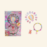 Hot Focus Dazzle Nails – Rainbow set shown with retail packaging, colorful glitter press-on nails, hot air balloon display piece, pastel bracelet with bear charm, small ring, and pink rainbow-themed artwork.