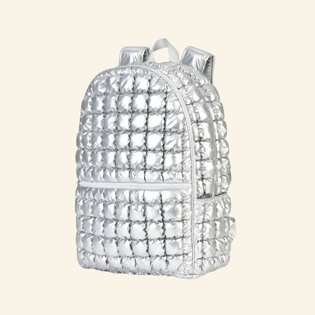 iScream Icy Silver Puffer Backpack shown from an angled side view, highlighting the metallic quilted puffer texture, side pocket, front zipper compartment, top handle, and padded shoulder straps.
