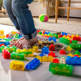 Colorful building blocks on a floor with a child's legs and feet in jeans.