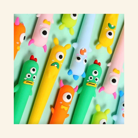 Close-up of Little Monster Gel Pens scattered together, showing colorful monster faces, horns, eyes, and expressive character details.