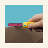 Hand using the yellow Makedo Safe-Saw to cut along a dotted line on cardboard, demonstrating the tool’s cardboard cutting function.