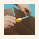 Close-up of a hand using the yellow Makedo Scru-Driver to connect a blue Scru through cardboard, with the pink Safe-Saw visible nearby.