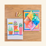 Rainbow Colors Sketchbook by eeBoo with colorful geometric cover beside an open sketchbook and oil pastels.