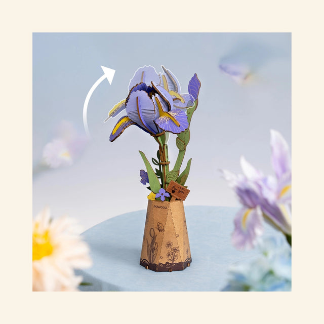 Completed Robotime Rowood Purple Iris wooden flower displayed in a small decorative vase on a soft blue surface, with an arrow showing the adjustable flower head angle.