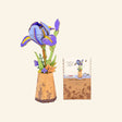 Robotime Rowood Purple Iris DIY Wooden Flower 3D Puzzle shown completed in a small illustrated paper-style vase beside the matching project card and packaging artwork.