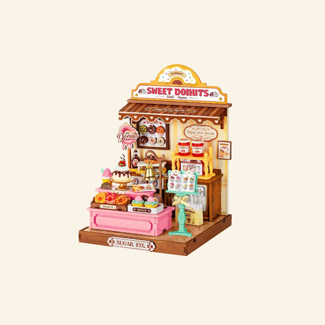 Rolife Sweetie’s Donut Shop completed miniature build shown from the front with pastel pink counter, donut displays, sweet shop signs, tiny accessories, and vintage bakery details.