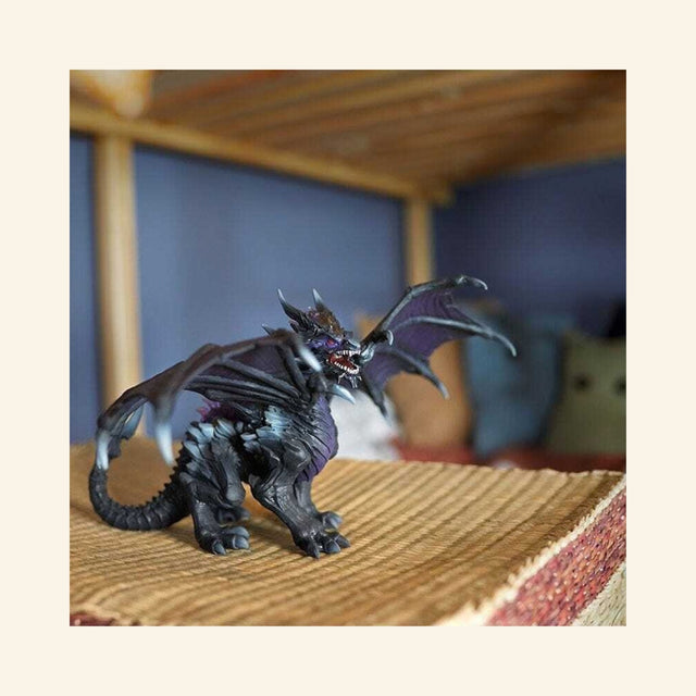 Schleich® ELDRADOR® Creatures Shadow Dragon shown in a play scene on a woven surface with wings extended and dark fantasy creature detailing.