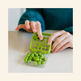Hands playing SmartGames IQ Mini in a green travel case, placing puzzle pieces into the compact board during a solo logic challenge.