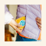 SmartGames IQ Mini yellow travel case tucked into a jacket pocket, showing the compact pocket-sized design for on-the-go play.