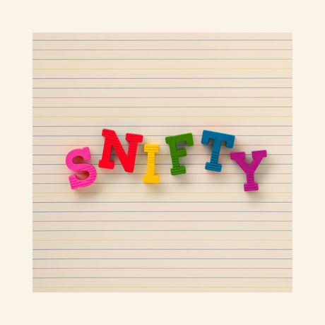 Snifty ABC Crayons arranged on lined paper to spell “SNIFTY” using bright red, pink, yellow, green, blue, and teal letter-shaped crayons.