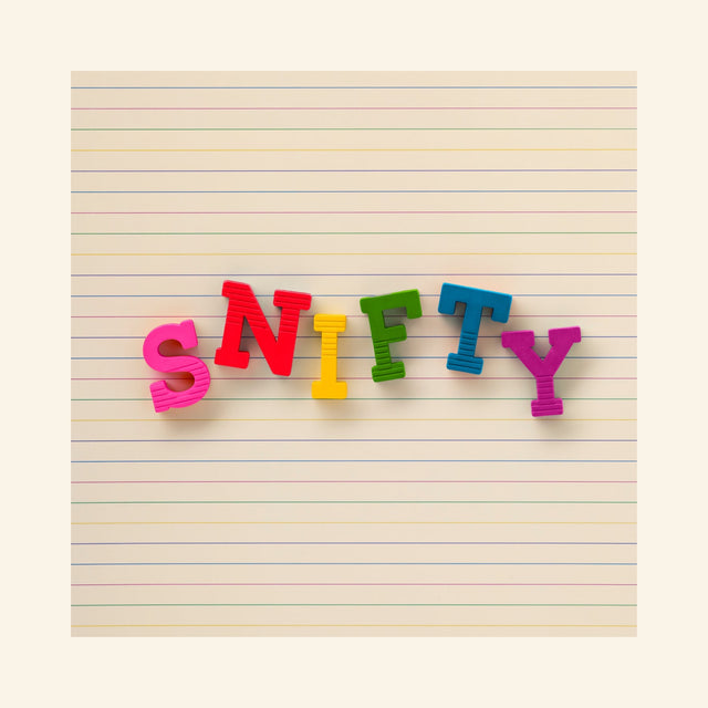 Snifty ABC Crayons arranged on lined paper to spell “SNIFTY” using bright red, pink, yellow, green, blue, and teal letter-shaped crayons.
