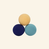Three Speks Odds Lines magnetic fidgets in cream, navy blue, and teal, featuring rounded shapes covered in fine ridged lines.