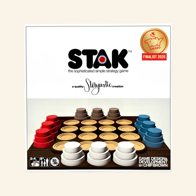 Storyastic STAK Strategy Game front box showing the elegant wooden game board, stacked red, white, brown, and blue pucks, STAK logo, Toy Award finalist badge, and sophisticated strategy game description.