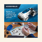 Thames & Kosmos Air-Power Turbo Racer assembly graphic showing the white air-powered race car, hands building wheel parts, instruction booklet, tools, tubing, and text that says to build an air-powered roaring racer from over 90 pieces.