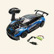 Ultimate Drift RC Car shown in blue-and-black racing style with large rear spoiler, 2.4 GHz remote control, rechargeable battery pack, and USB charging cable displayed beside the car.