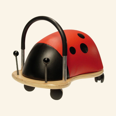 Small Wheely Bug Ladybug ride-on toy with a red-and-black padded ladybug body, curved black push handle, wooden base, black antennae, and small caster wheels.